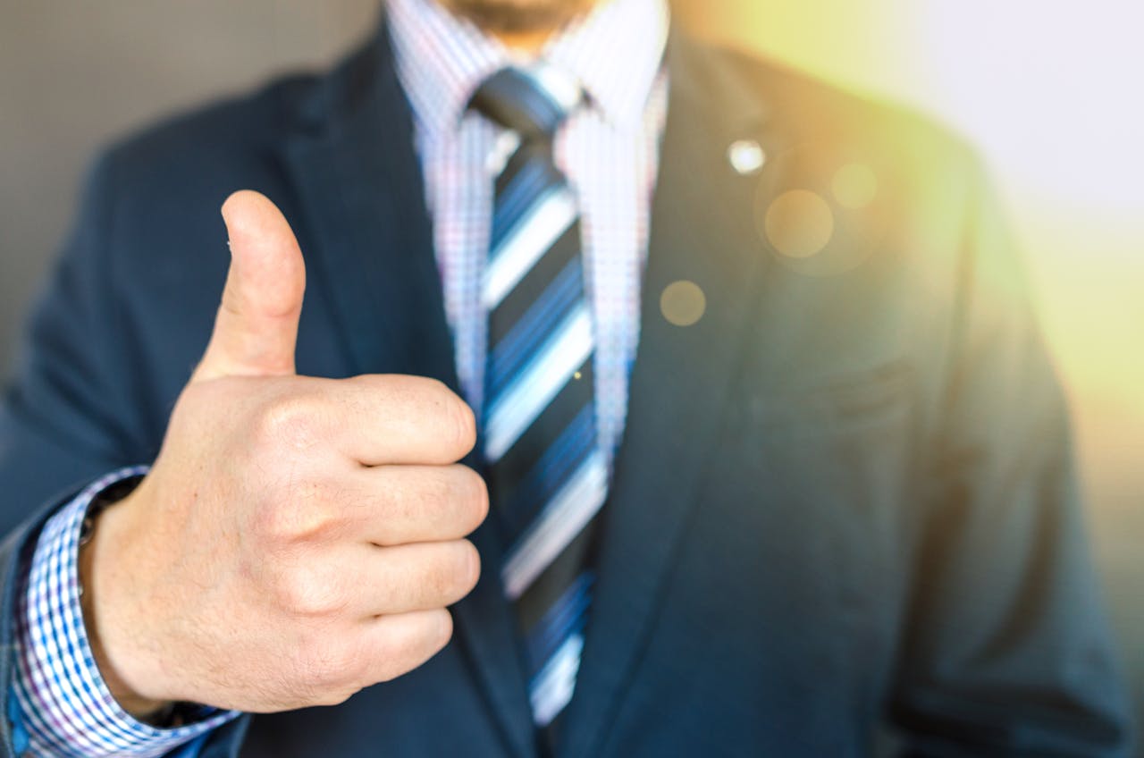 Close-up of a businessman in a suit giving a thumbs-up in a bright, positive setting.
